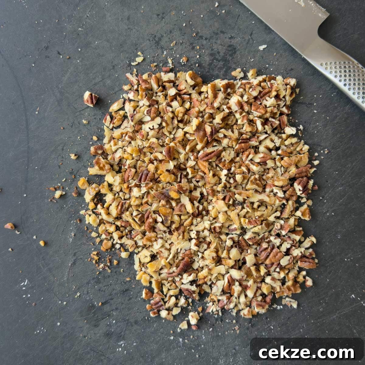 Chopped nuts on a black cutting boards with a chef's knife.