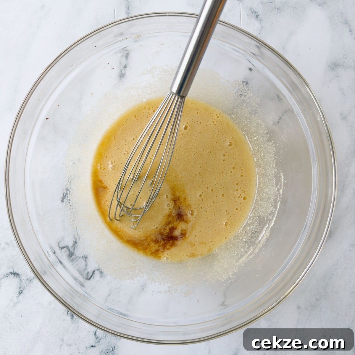 Whisking eggs and sugar in a glass bowl with vanilla extract.