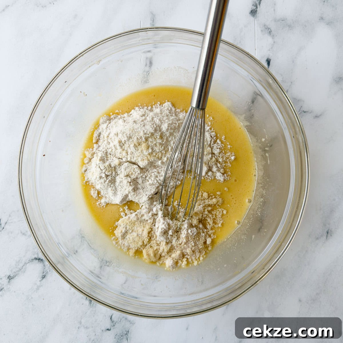 Mixing batter for a Nantucket cranberry pie in a glass bowl with silver whisk.