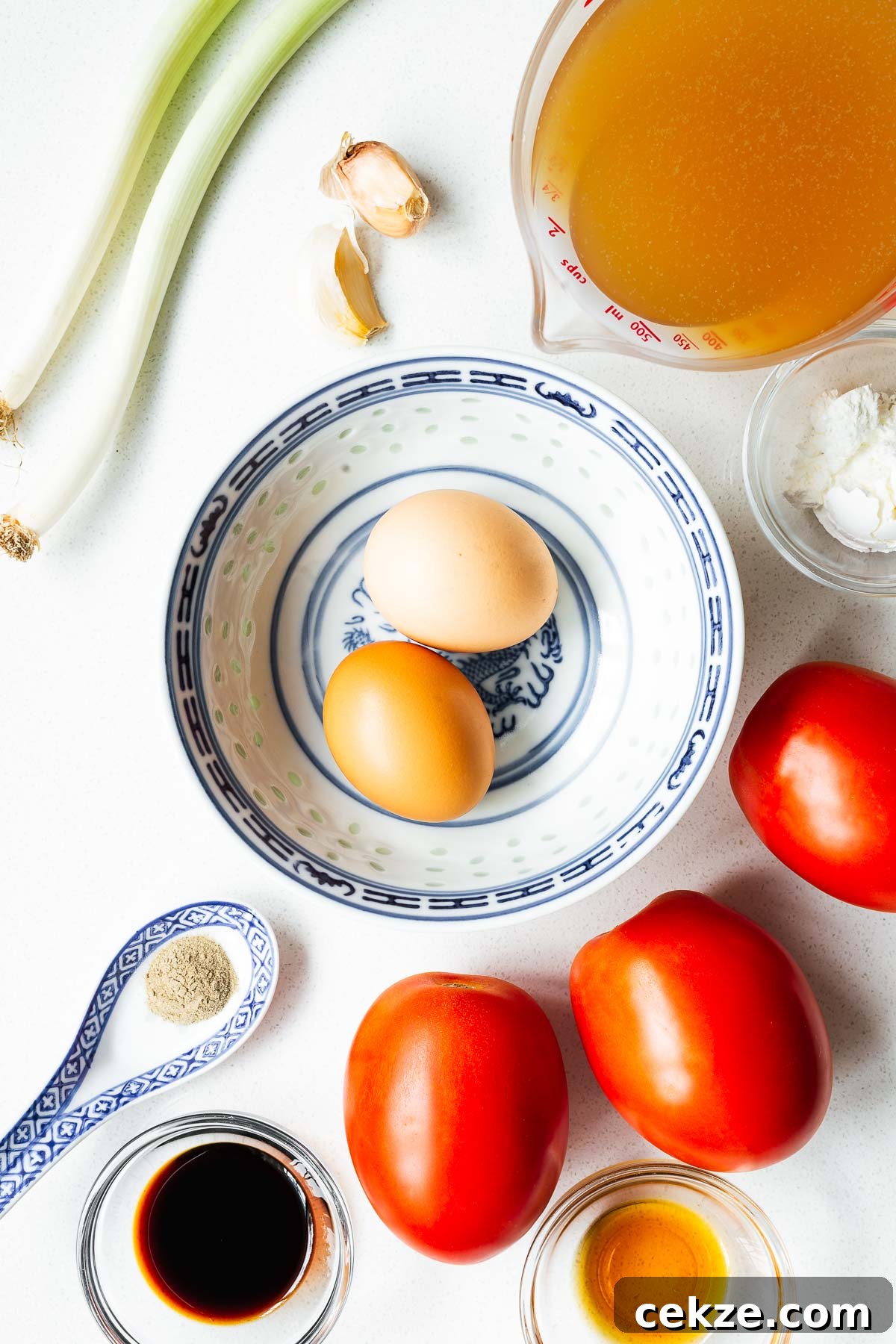 Ingredients for tomato egg drop soup arranged on a white kitchen counter viewed from above.