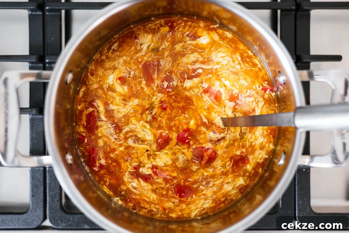 A soup pot with delicate egg flowers in a tomato-based broth.