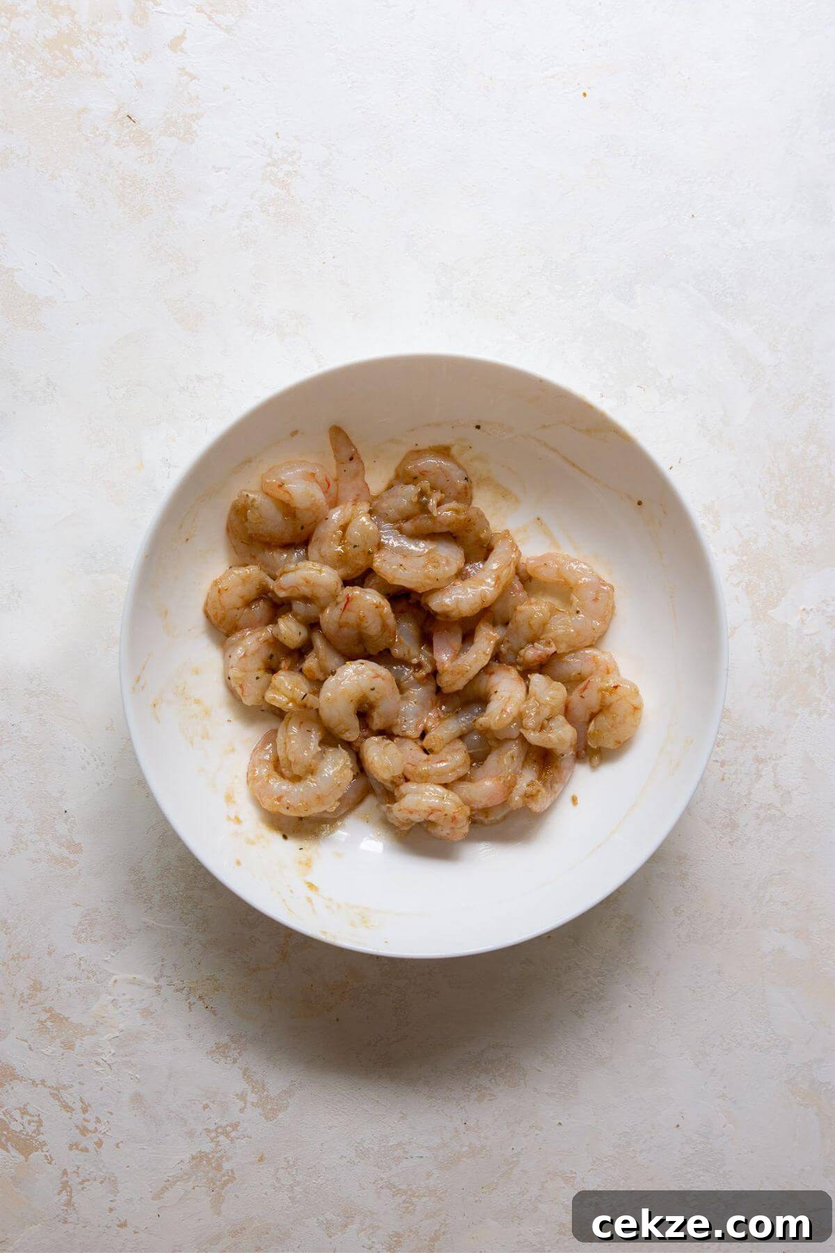 Raw shrimp tossed with garlic and balsamic dressing, marinating in a white bowl.