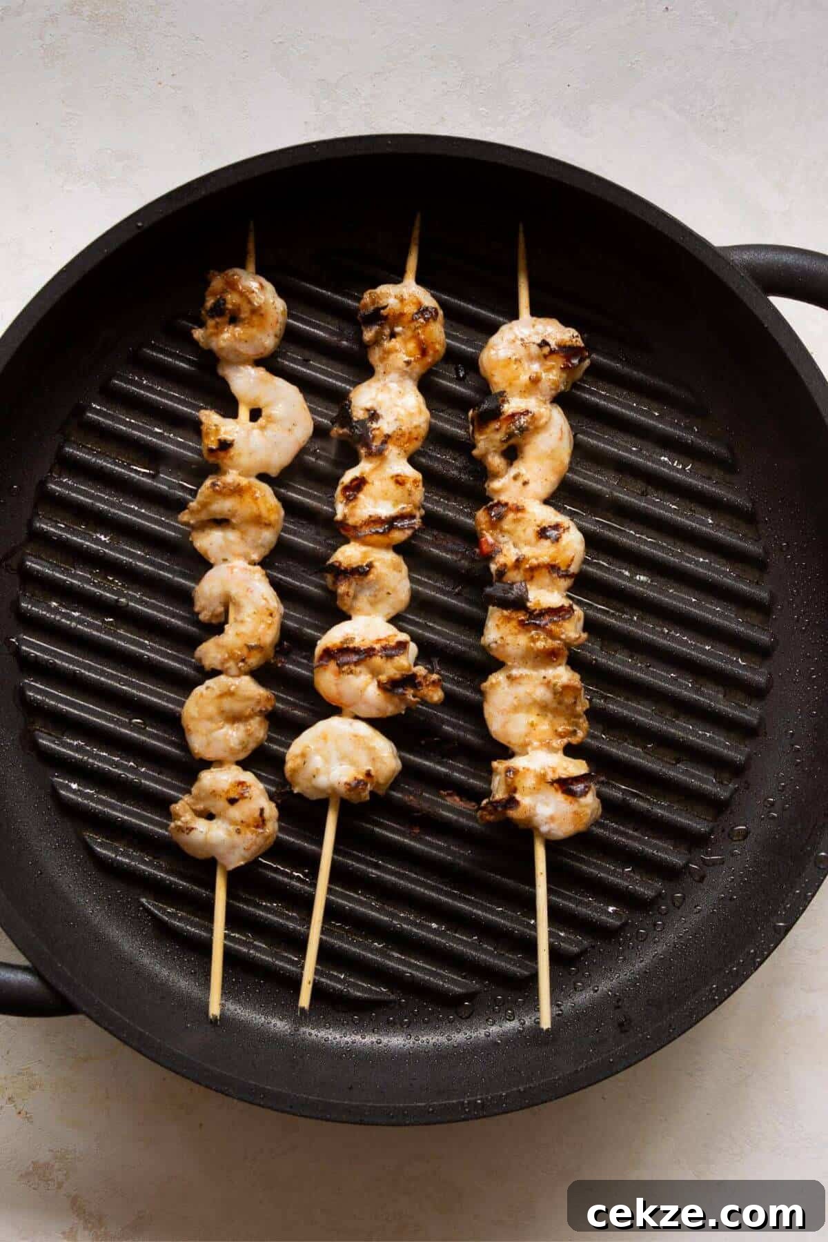 Shrimp threaded onto skewers and grilling on a cast iron grill pan.