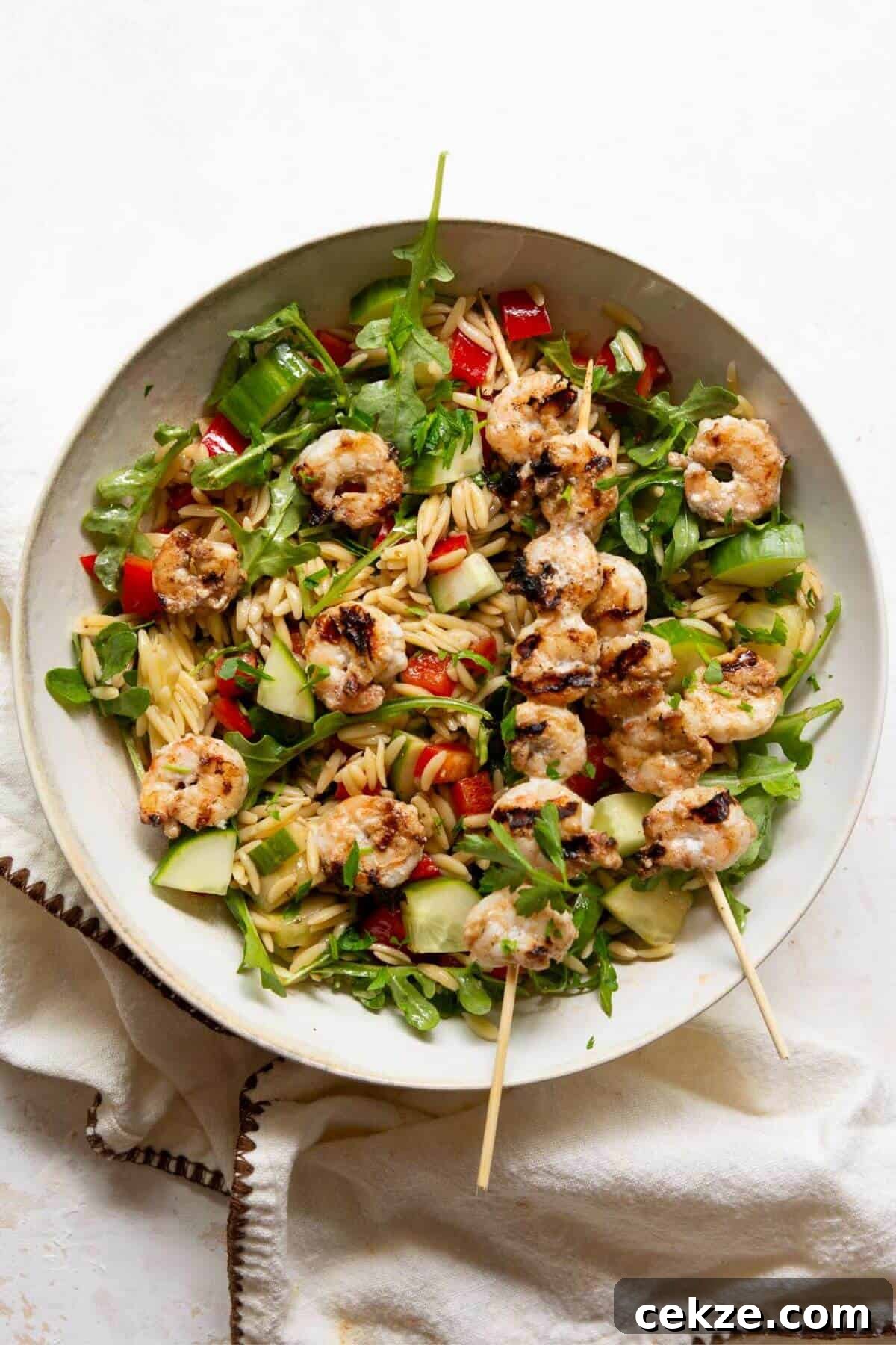 Finished grilled shrimp orzo salad plated with skewers, arugula, and fresh parsley.