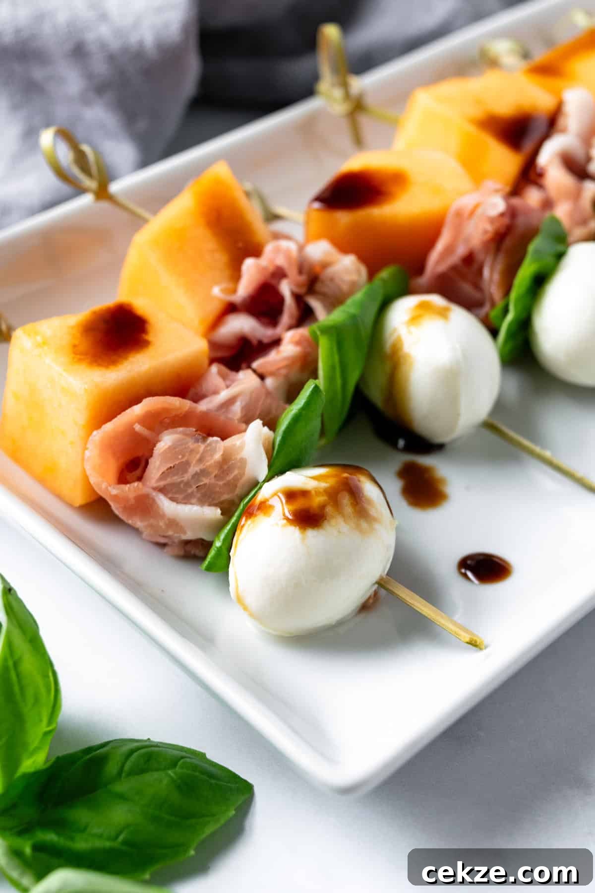 Prosciutto and Melon Skewers: Sweet-Salty Appetizer Recipe 2 Prosciutto Melon Skewers on a white plate.