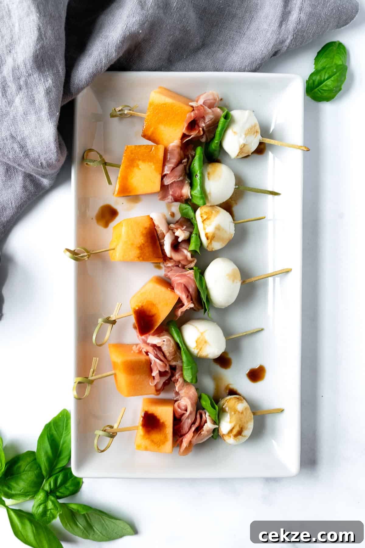 Prosciutto and Melon Skewers: Sweet-Salty Appetizer Recipe 5 A white plate of melon prosciutto skewers.
