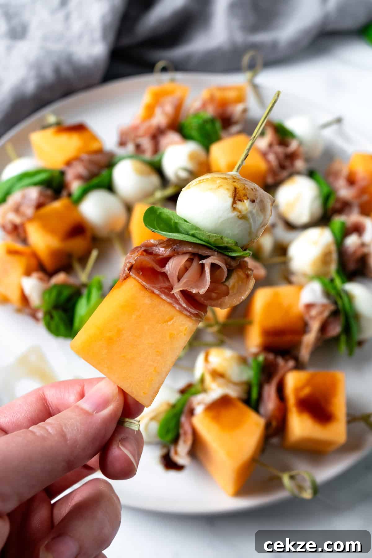 Prosciutto and Melon Skewers: Sweet-Salty Appetizer Recipe 6 Hand holding a prosciutto melon skewer.