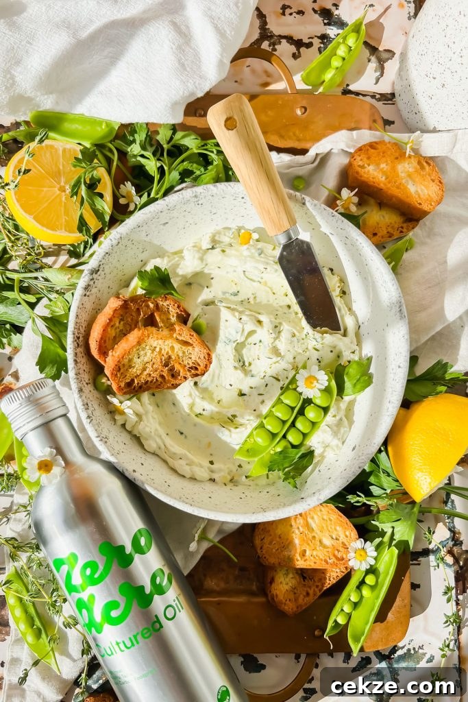 Feta, Bacon & Date Dip Recipe: Sweet Savory Party Appetizer 12 cream cheese garlic dip in white bowl with two toasted crostinis and pea pods in bowl beside bottle of zero acre cultured oil with fresh herbs surrounding.