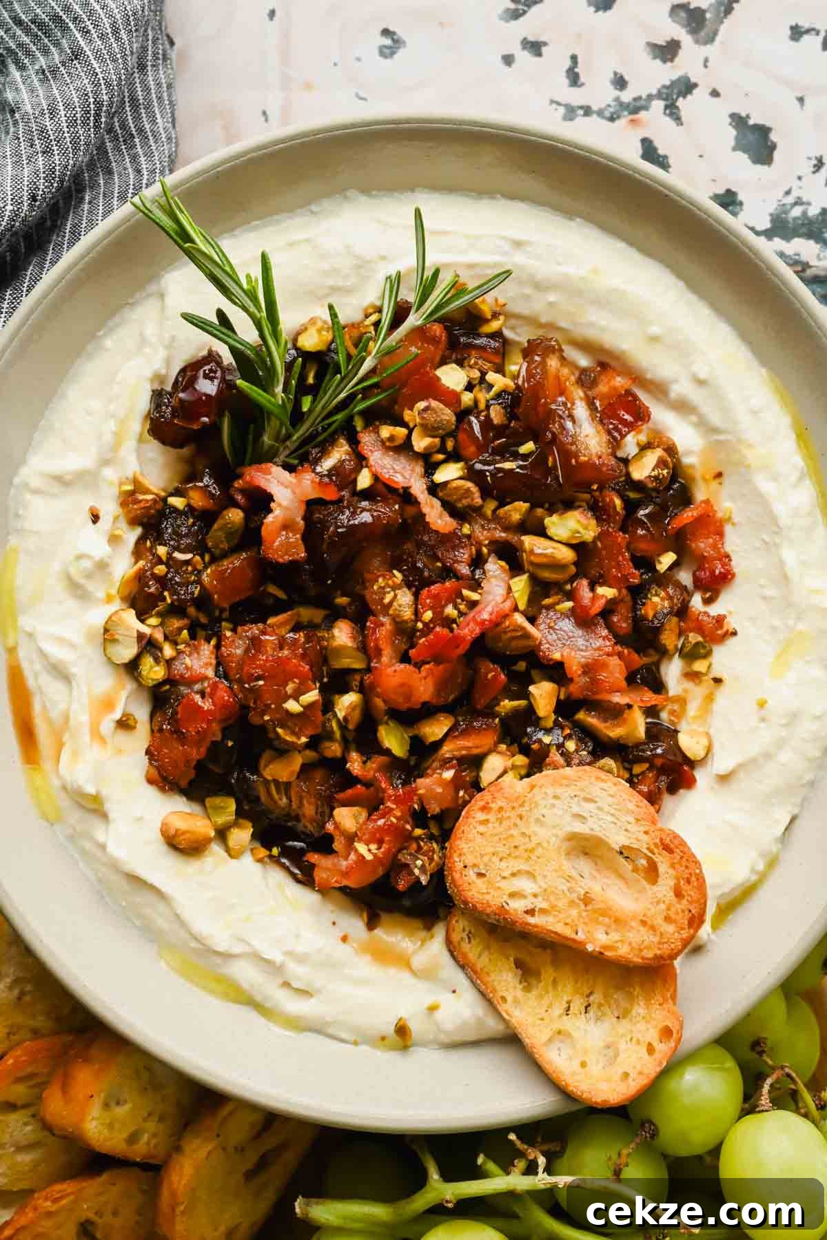 Feta, Bacon & Date Dip Recipe: Sweet Savory Party Appetizer 7 serving bowl with whipped feat cheese topped with a date, bacon, pistachio mixture garnished with rosemary.