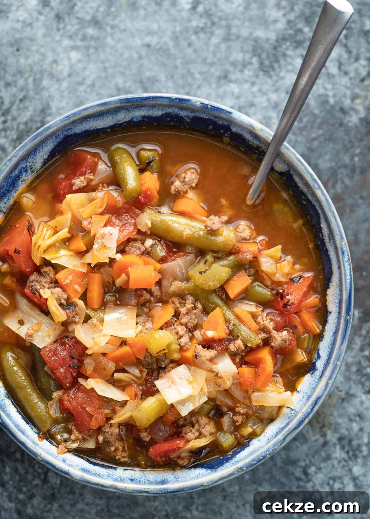 Cabbage and Beef Hamburger Soup Recipe for Comforting Meals 2 overhead image of hamburger soup with cabbage in a blue bowl with a spoon