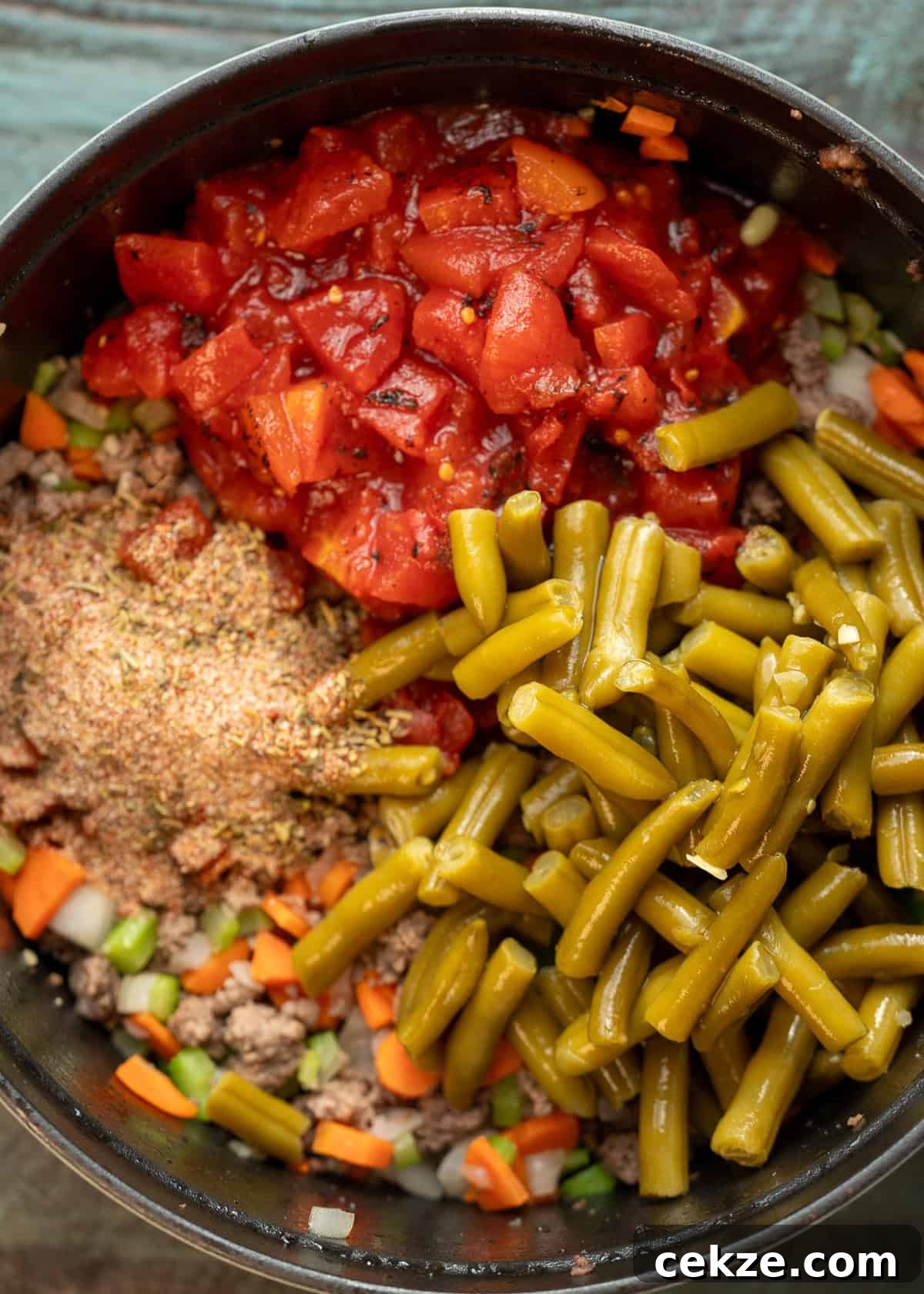 Cabbage and Beef Hamburger Soup Recipe for Comforting Meals 5 green beans and tomatoes being added to hamburger soup with cabbage in black dutch oven