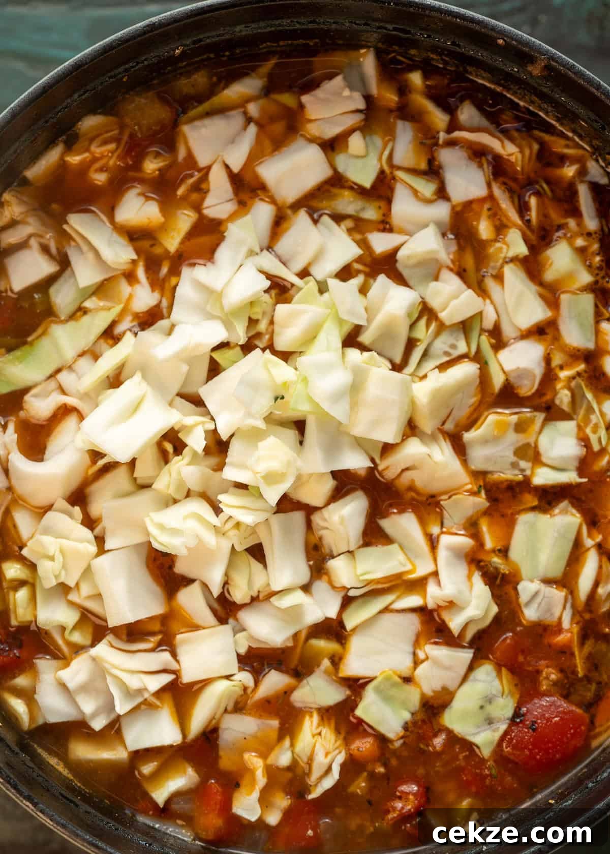 Cabbage and Beef Hamburger Soup Recipe for Comforting Meals 6 overhead image of broth and cabbage being added to hamburger soup with cabbage in black dutch oven