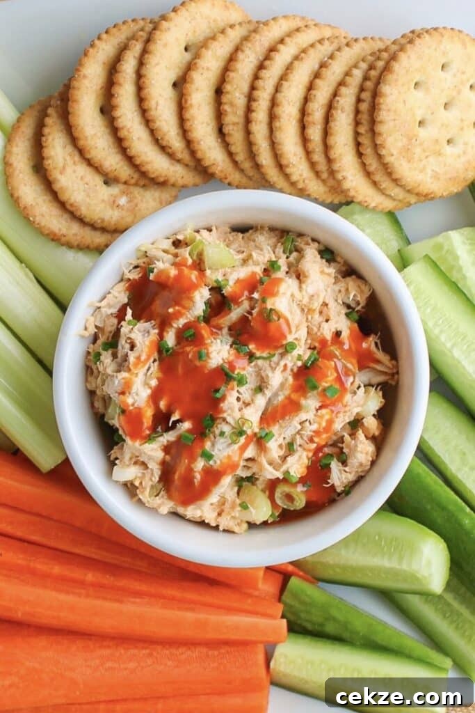 Buffalo chicken salad in a white bowl with crackers and sliced veggies.