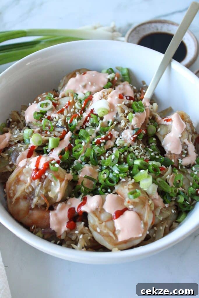 Shrimp egg roll in a bowl topped with a spicy creamy sauce and sriracha.
