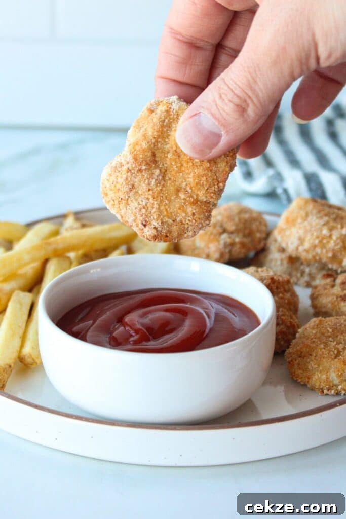 A homemade baked ground chicken nugget being dipped into ketchup.