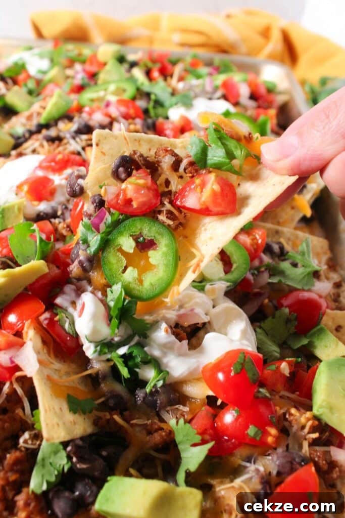 A close up shot of loaded ground turkey nachos with one chip being picked up from the sheet pan.