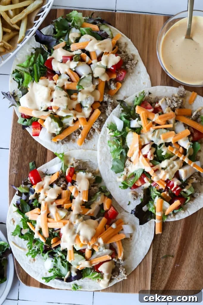 Big mac wraps on a wooden board drizzled with big mac sauce and served with french fries.