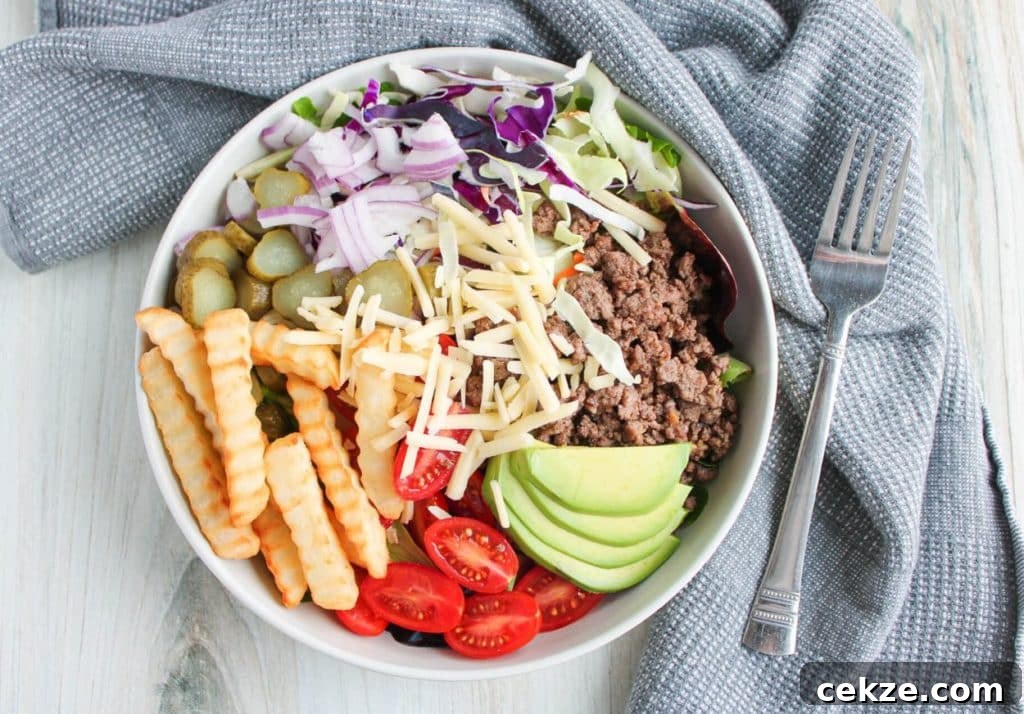 A deconstructed burger salad bowl on a countertop with a napkin and fork.