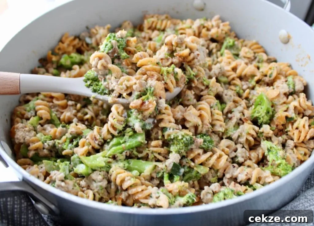 Ground turkey alfredo pasta with broccoli in a pan, with a large serving spoon scooping out a spoonful.