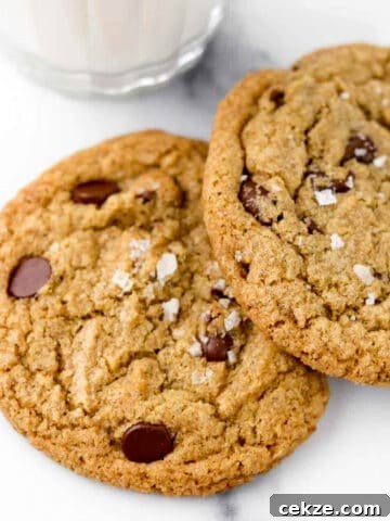 Close up of Rye Chocolate Chip Cookies sprinkled with sea salt next to a glass of milk.