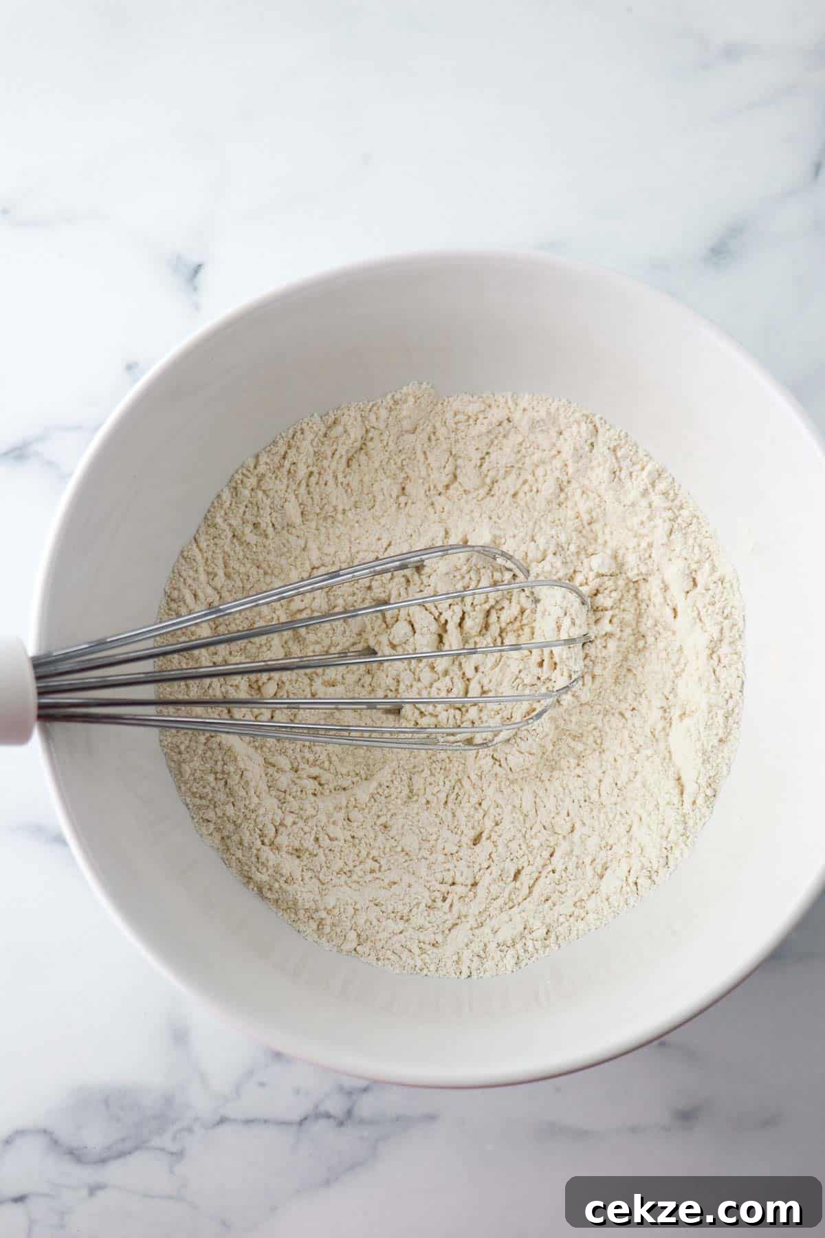 Dry ingredients in a white bowl with a whisk.