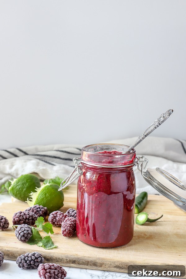 blackberry enchilada sauce in a glass jar on a wood cutting board surrounded by blackberries, lime, and cilantro