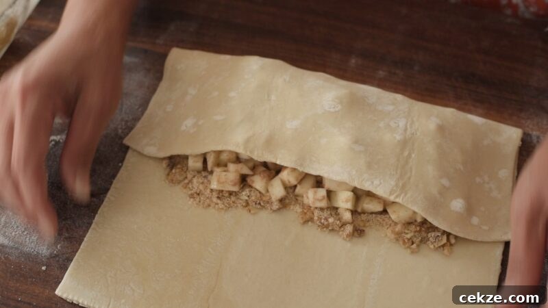 Folding puff pastry dough over apple filling to form the strudel