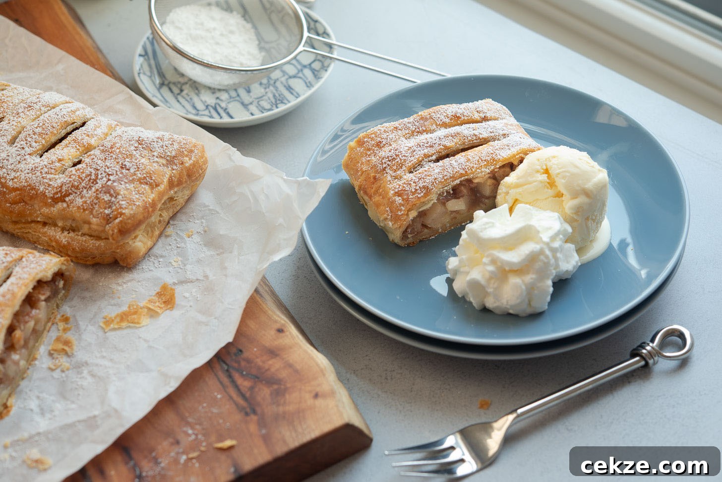 A slice of apple strudel served with ice cream and whipped cream on a plate