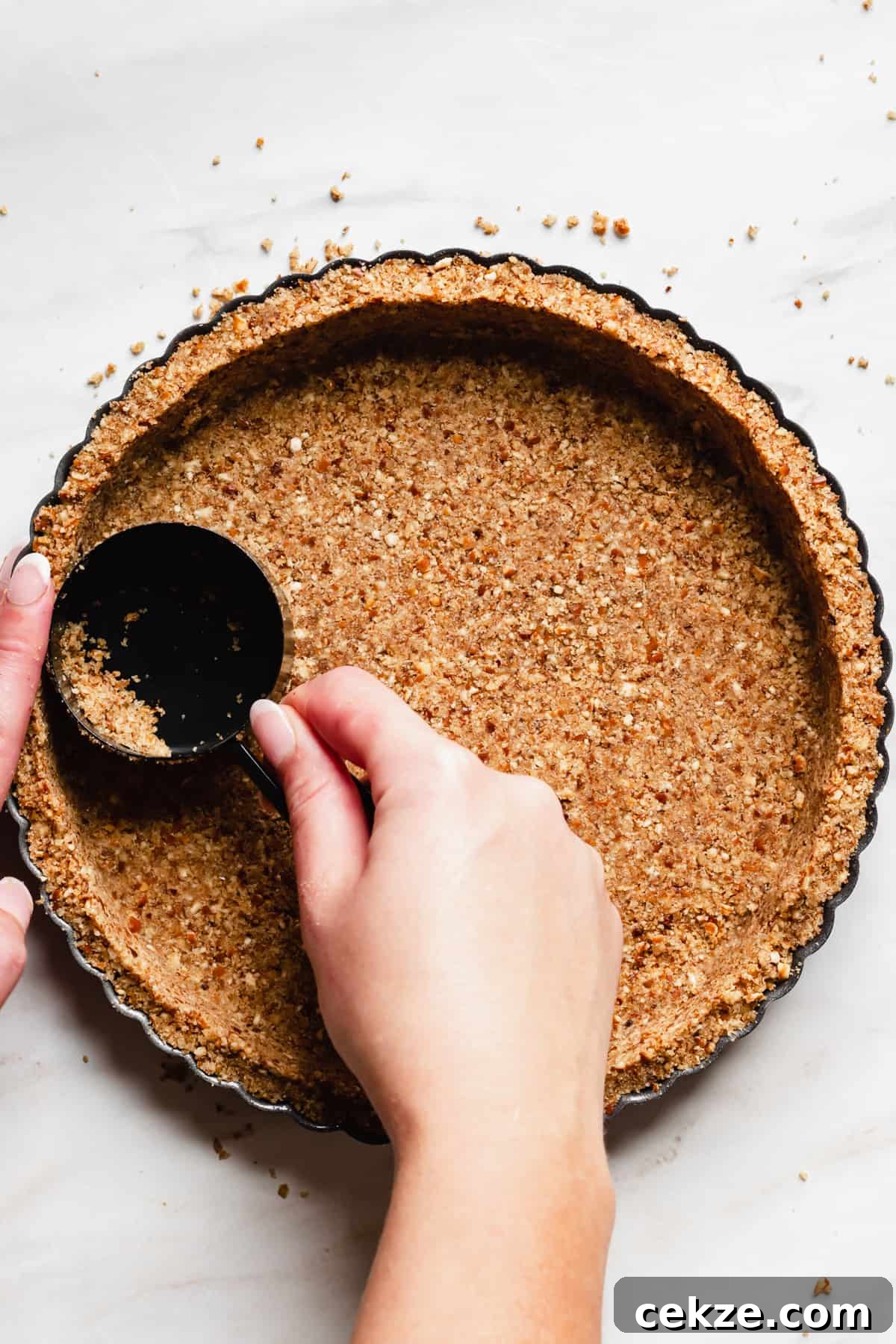 Pretzel crumbs being pressed into a tart pan with a measuring cup