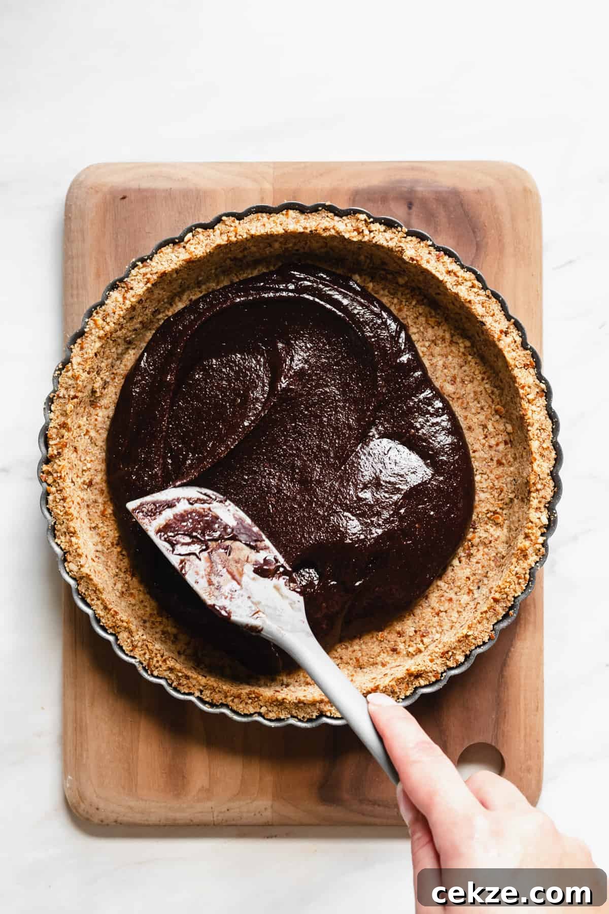 Brownie batter being spread to meet the edges of the crust