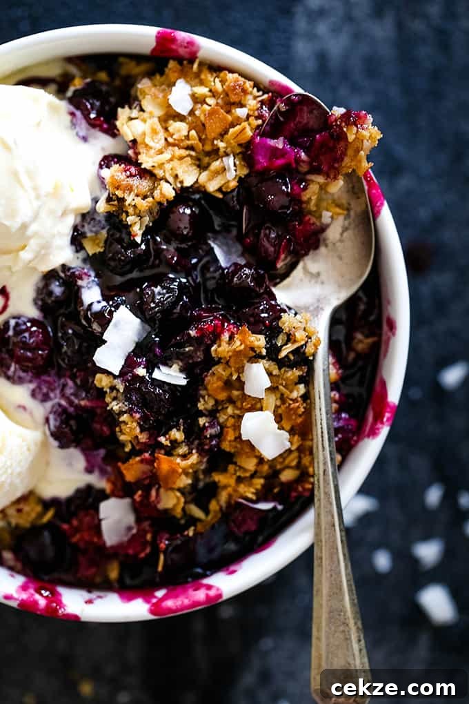 It takes just 15 minutes to prepare this delicious Coconut Blueberry Crisp featuring warm, bubbly blueberries capped by a crunchy cap of oats and coconut. Coconut Blueberry Crisp in a white bowl topped with ice cream and a spoon.