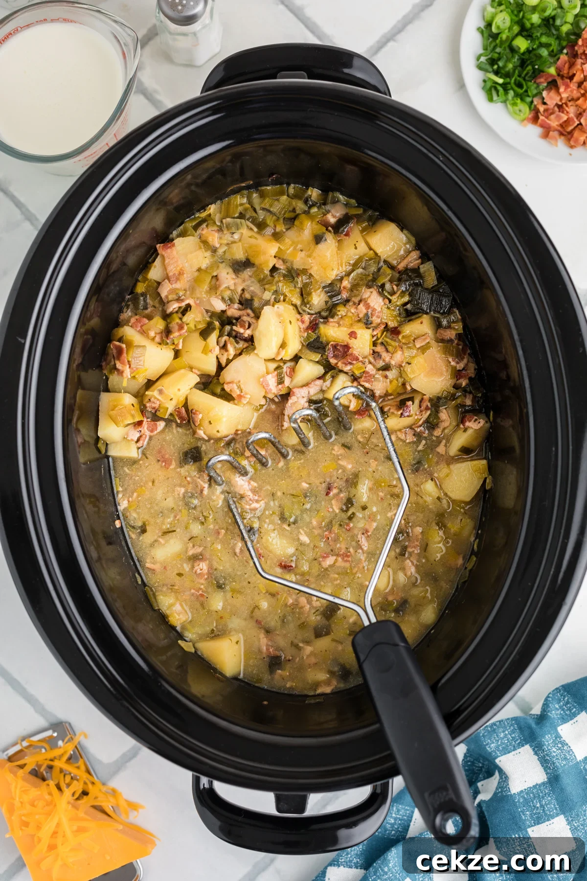 Smashing cooked potatoes in a crockpot with a potato masher.