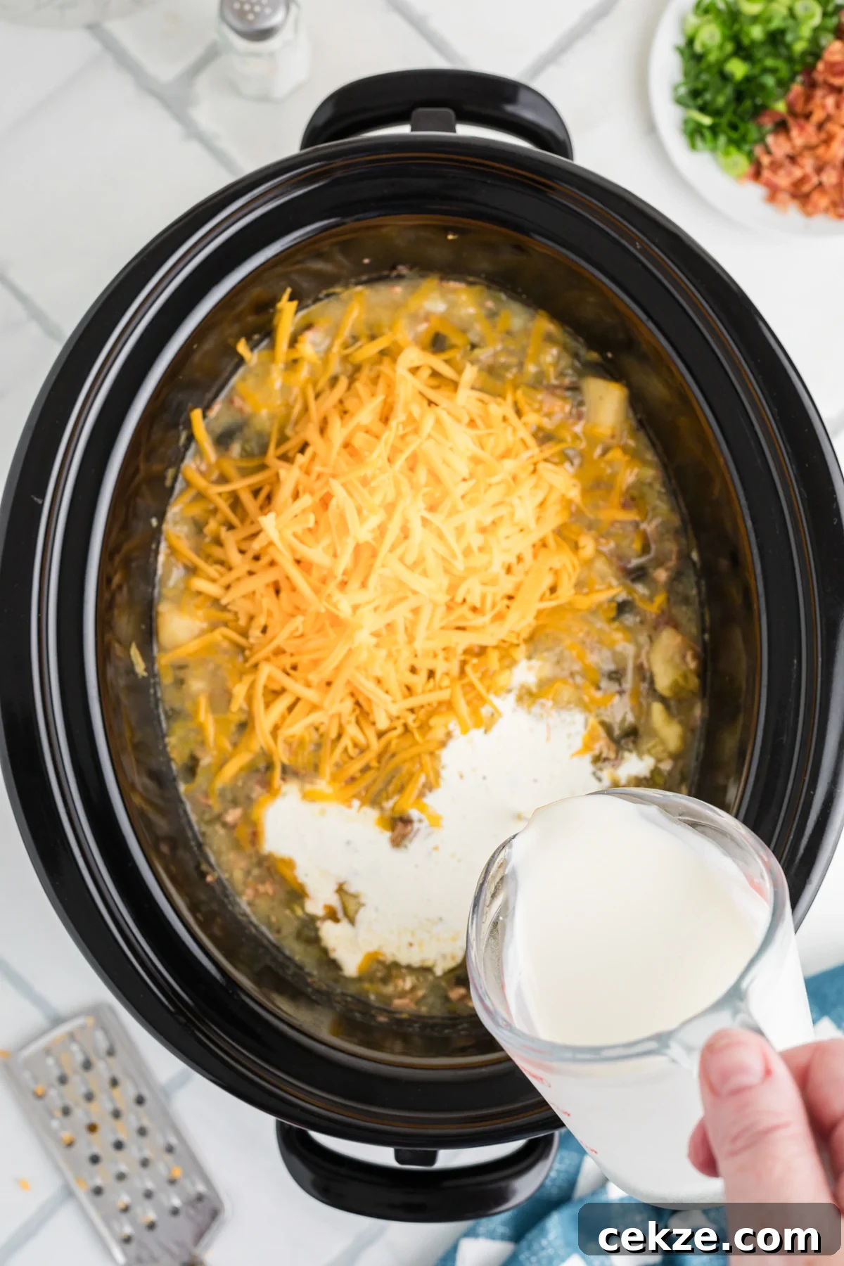 Pouring heavy cream into a crockpot after adding cheese.