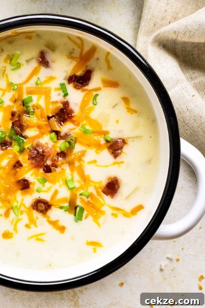 Close-up of creamy loaded potato soup in a white bowl with crispy bacon, shredded cheddar cheese, and sliced green onions on top.