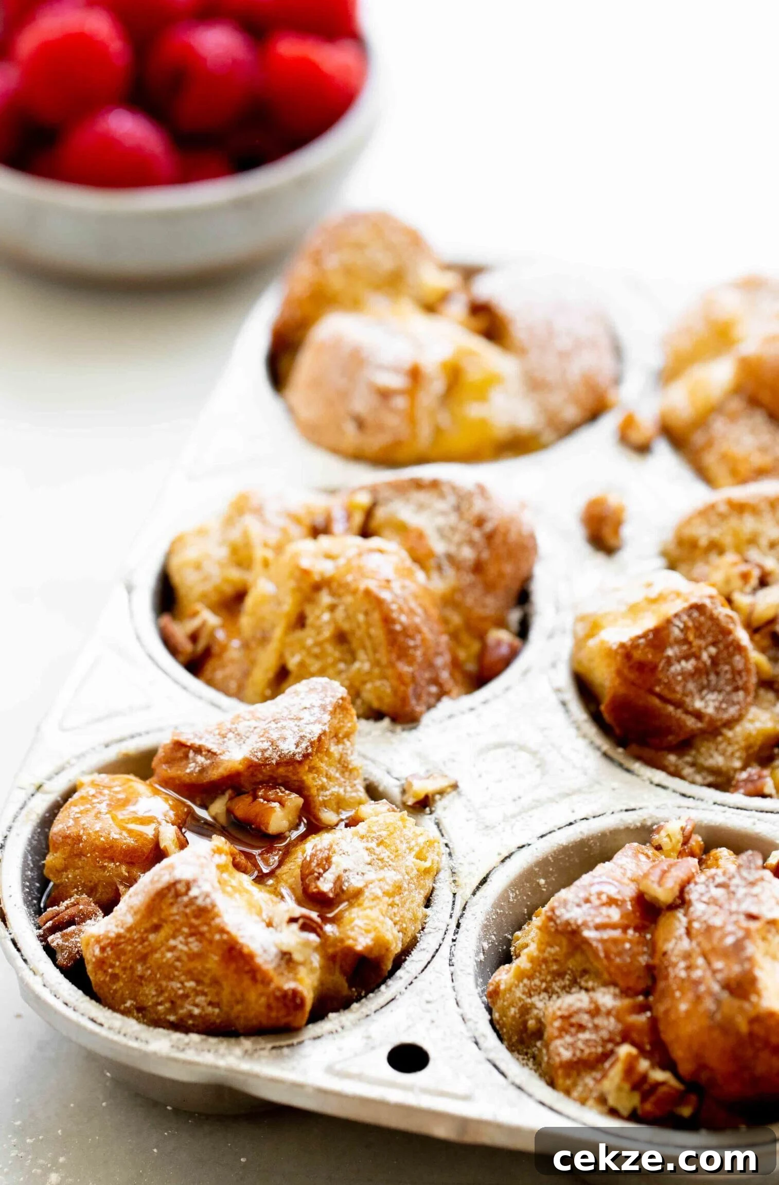 closeup photo of french toast muffins in aluminum muffin tin with a bowl of raspberries in the background