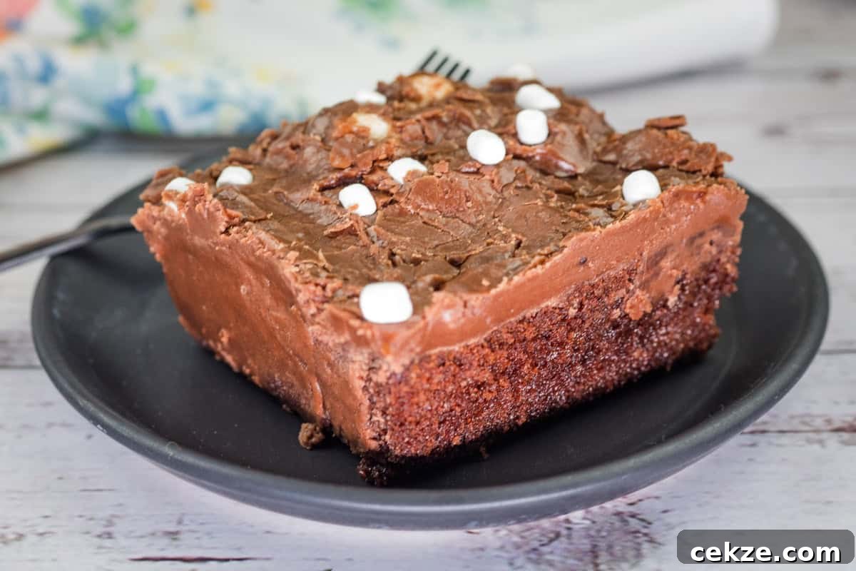 A slice of Grandma's Coca-Cola cake with chocolate frosting and small marshmallows on a black plate.