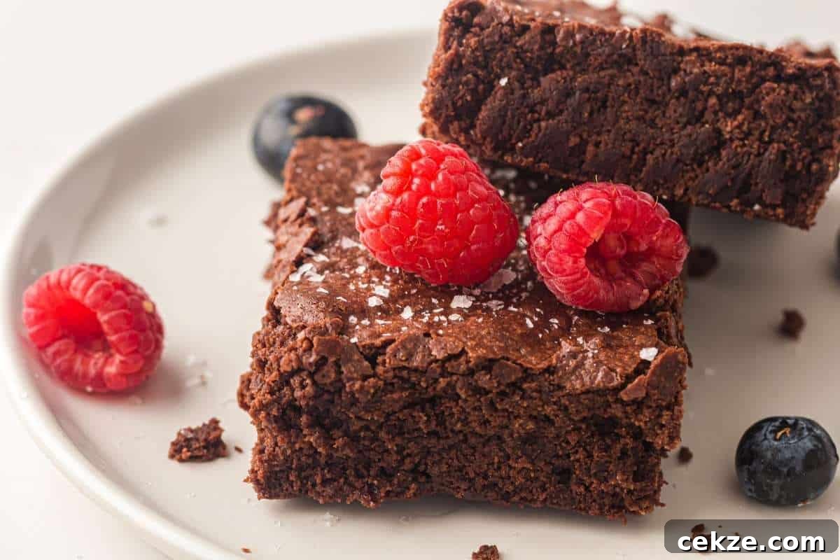 Two Sheet pan chocolate brownies on a white plate, topped with raspberries and a sprinkle of sea salt, with additional raspberries and blueberries on the side.