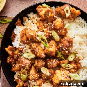 crispy air fryer sesame chicken atop a bed of white rice topped with green onions