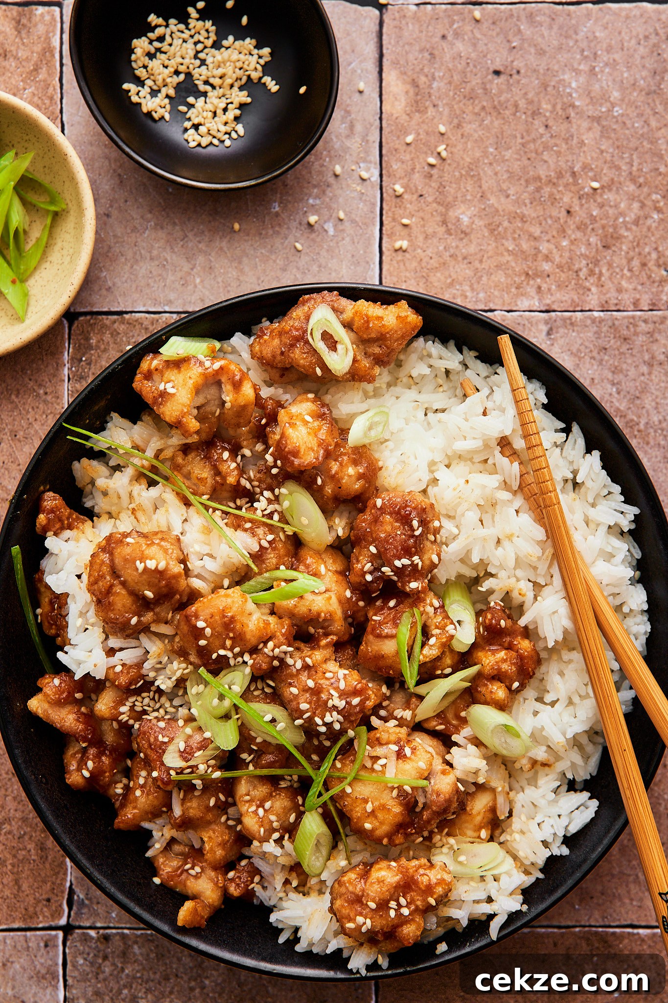 air fryer sesame chicken atop a bowl of fluffy white rice topped with scallions and sesame seeds 
