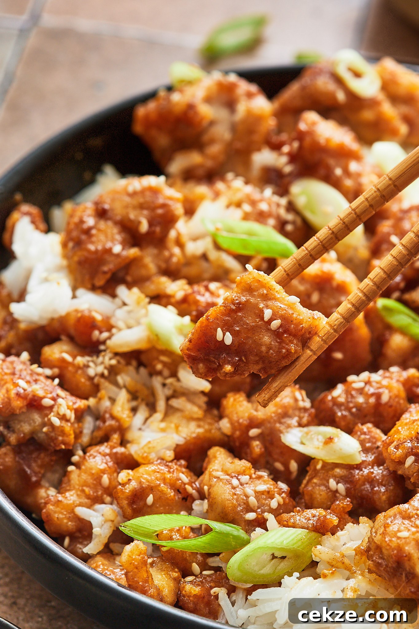 chopsticks picking up a piece of crispy sesame chicken 
