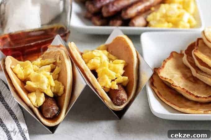 Two breakfast tacos in holders loaded with eggs, sausage, and syrup.
