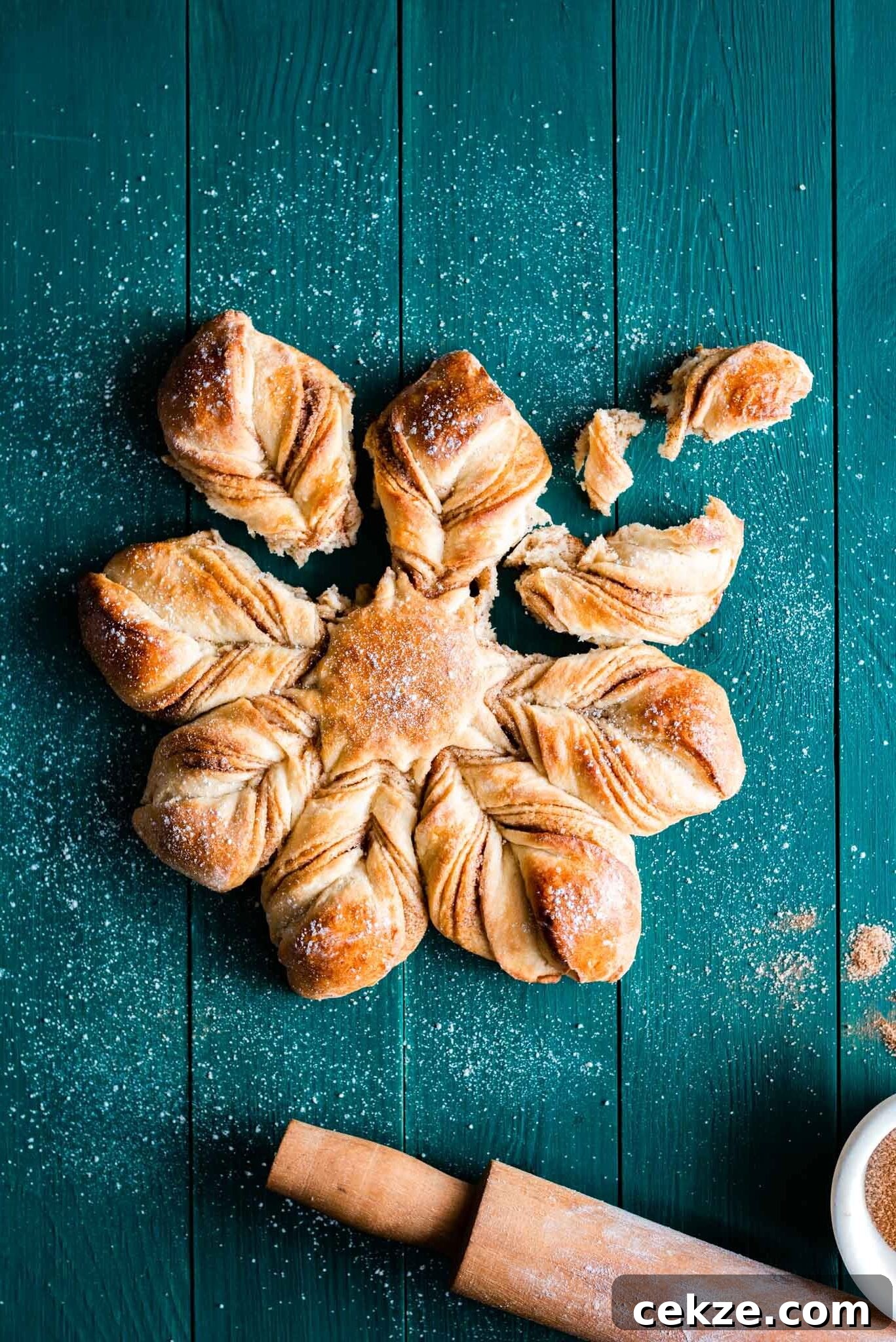 A star shaped bread with cinnamon filling on a table next to a rolling pin.