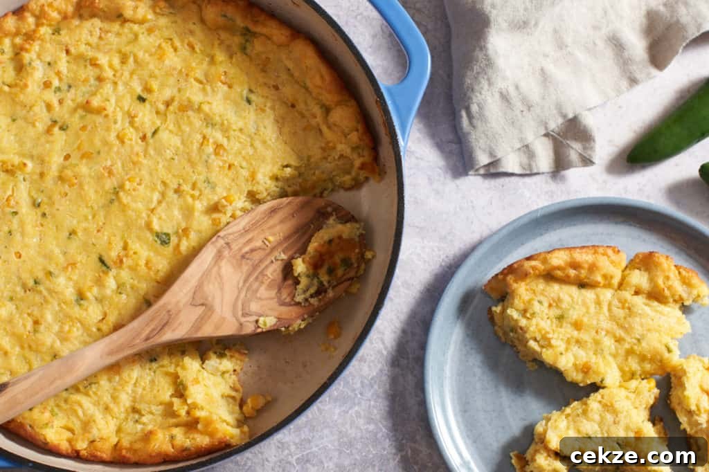 A casserole pan and a plate of spoonbread with a napkin and jalapeños in the background.