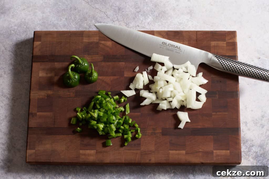 A knife on a cutting board with chopped onions and jalapeños.