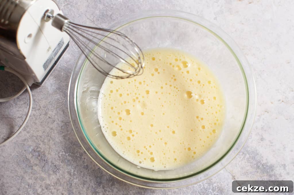 A hand mixer next to a bowl of whisked eggs.