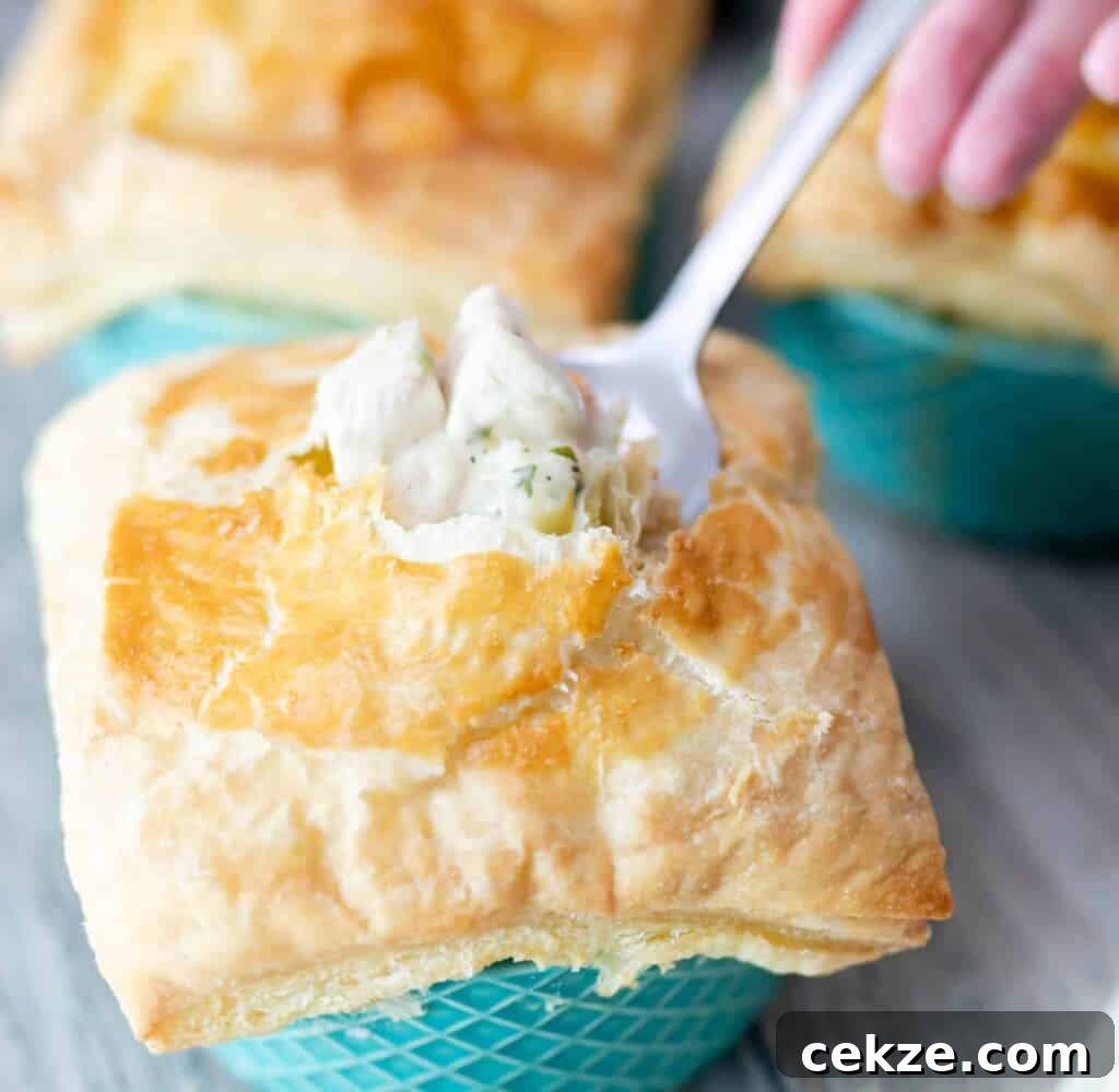A fork stuck inside of the chicken pot pie topped with puff pastry showing chicken in broth with seasonings.