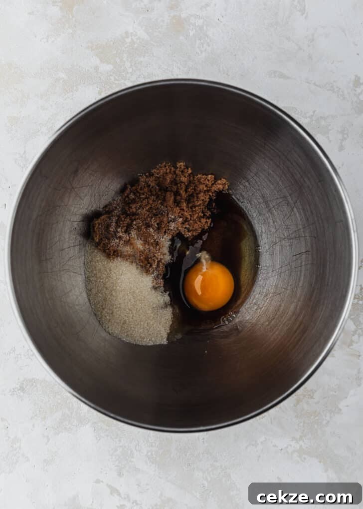 A silver bowl of white sugar, brown sugar, and an egg on a tan counter.