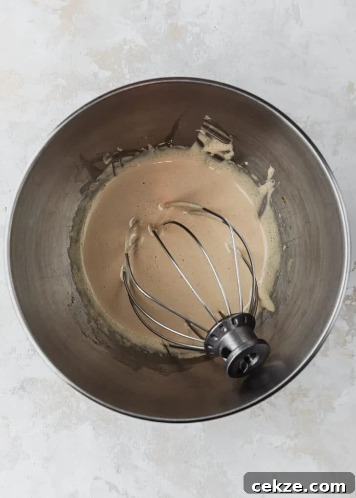A silver bowl with whipped eggs and sugar on a beige counter.