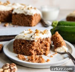 square slice of zucchini spice cake on a plate with a bite taken out of it by a fork.