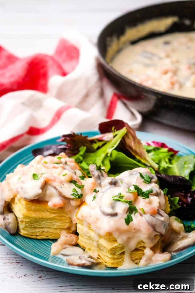 A plate of shrimp and mushroom vol-au-vents with sauce in pan in the background.